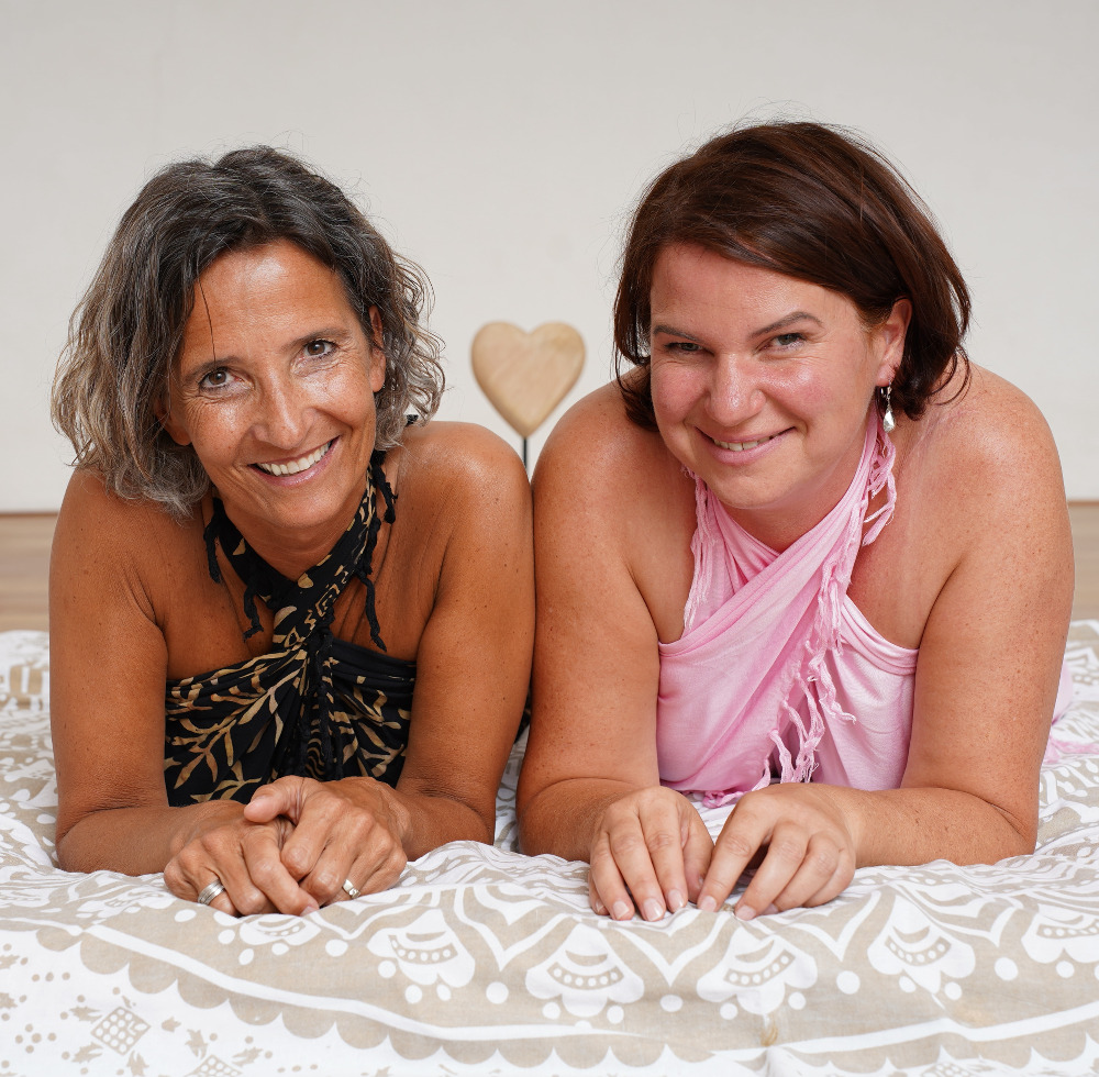 Zwei Frauen, auf dem Bauch liegen, von vorne fotografiert, lachend