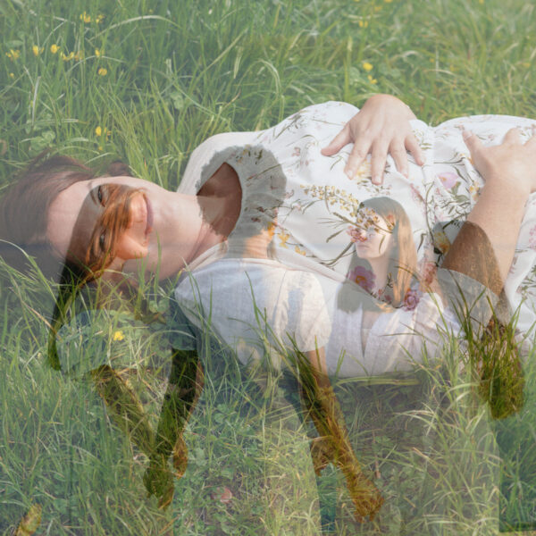 Frau liegt auf dem Rücken im Gras, Hände auf Brust und Bauch